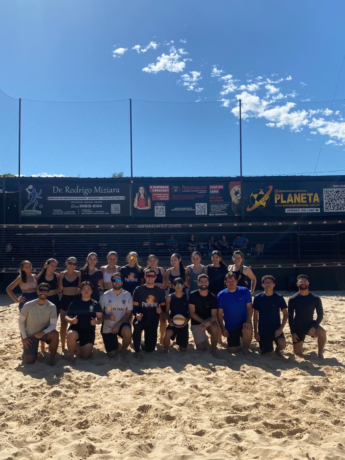 Turma de vôlei de praia posando na quadra em um dia de sol