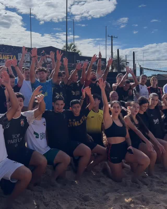 Alunos comemorando com os braços para cima na areia
